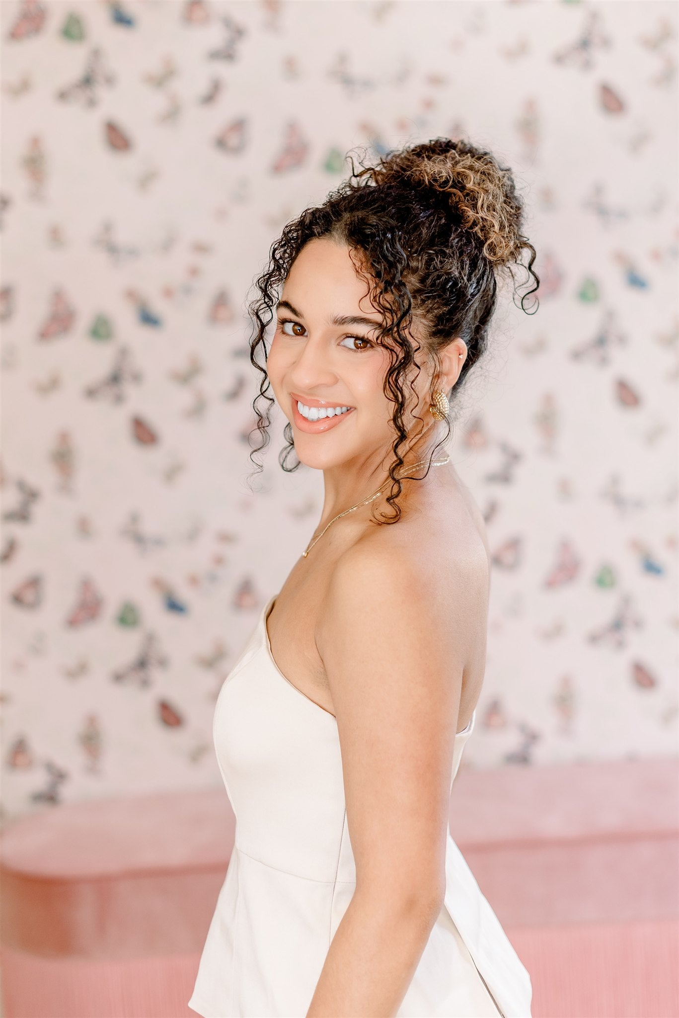 Woman in a white dress standing in front of a decorative wall with a pink couch.