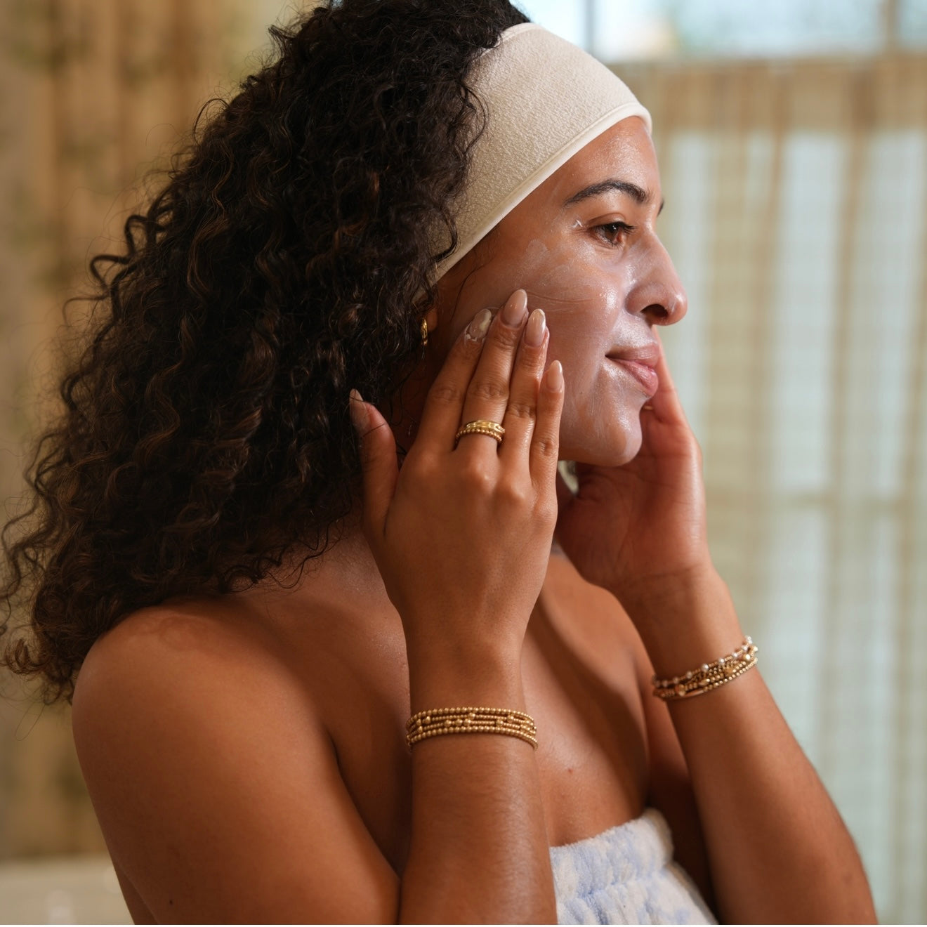 Woman applying cream to her face with a neutral background