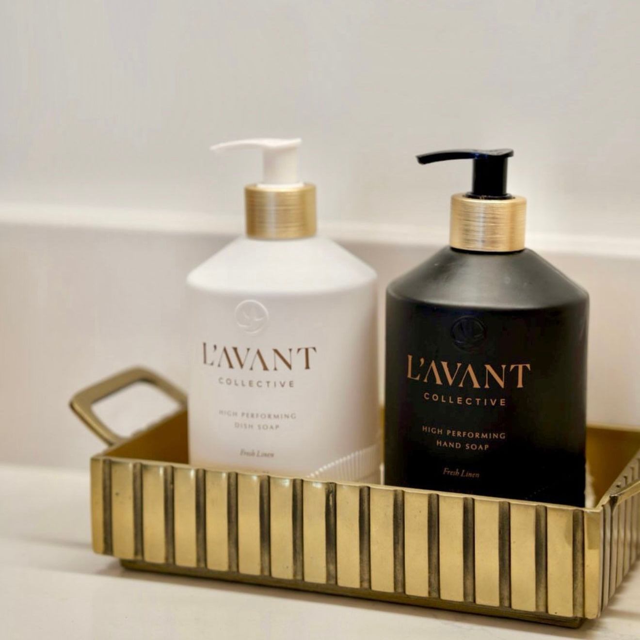 Two bottles of L'Avant Collective soap in a gold tray on a light background